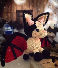 a crocheted bat stuffed animal sitting on top of a wooden stump in the snow