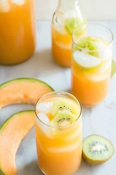 two glasses filled with orange juice, kiwi slices and watermelon wedges