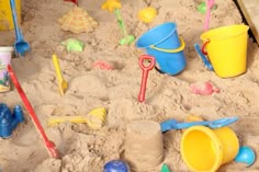 there are many toys in the sand with shovels and buckets on it's side