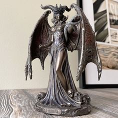 a statue of a woman with wings on top of a table next to a framed photo