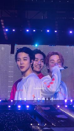 three young men standing next to each other in front of a large screen with lights on it