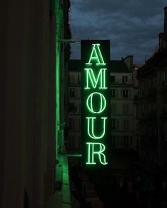 a green neon sign that says amour on the side of a building at night