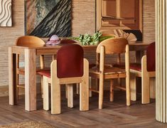 a dining room table with red chairs and a painting on the wall behind it,