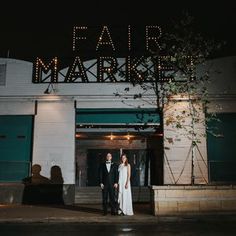 a bride and groom standing in front of the fair marquee sign at night