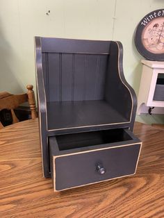 an old fashioned desk with a drawer and clock on the wall in the back ground