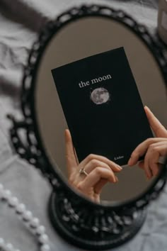 a person holding up a black book in front of a mirror with the moon on it