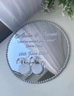 a personalized mirror with two wedding rings on it and flowers in the reflection behind it