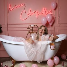 a woman sitting in a bathtub with pink balloons and holding a bottle of booze