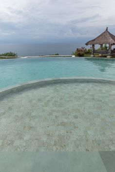 an empty swimming pool with thatched umbrellas on the roof and water in the foreground