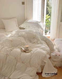 an unmade bed with white comforters and pillows on the floor next to a window