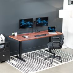 a desk with two monitors and a laptop on it in front of a gray wall