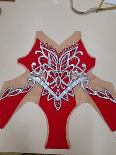 a red and white paper cut out with some silver beads on the top, sitting next to a pair of scissors