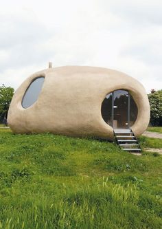 a house made out of concrete sitting on top of a lush green field with stairs leading up to it