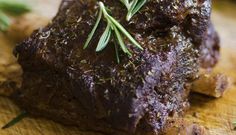 a piece of meat on a cutting board next to a knife and some fresh herbs