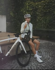 a woman sitting on a bench next to a bike eating an ice - cream cone