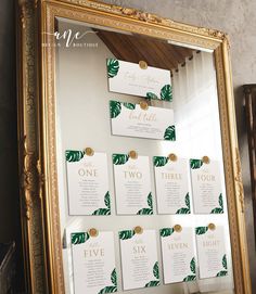 a gold framed mirror with place cards attached to the wall and hanging from it's sides