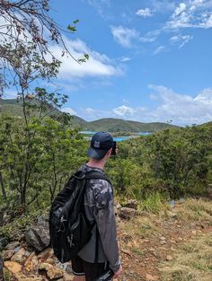 a man standing on top of a hill looking out at the trees and water in the distance