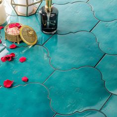 a blue tile floor with red rose petals on it and two bottles next to it