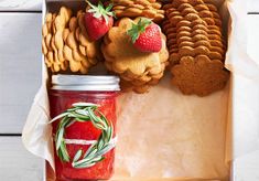 a box filled with cookies, jam and strawberries next to crackers on a table