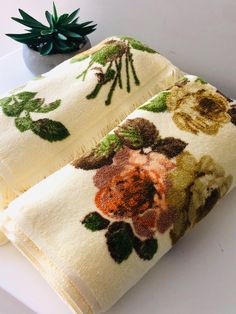 two white towels with flowers on them next to a potted succulent plant