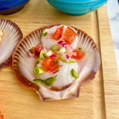 two scallop shells on a cutting board with other food items