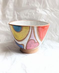 a colorful bowl sitting on top of a white sheet covered table next to a wall