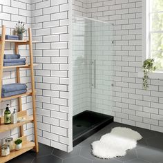 a white tiled bathroom with black and white tile on the floor, shelving unit for towels