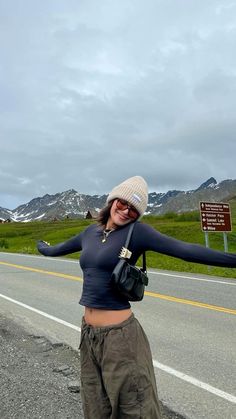 a woman standing on the side of a road with her arms outstretched in front of her