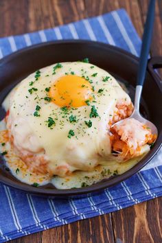 a black plate topped with an egg covered in gravy next to a fork