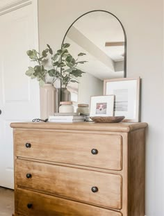 a dresser with a mirror, plant and pictures on it