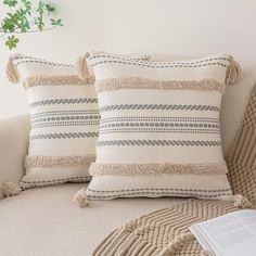 two pillows sitting on top of a couch next to a pillow with tassels