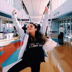 a woman standing in an airport holding her arms up and smiling at the camera,