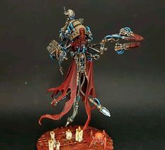 a red and white painted warhammer figure on a wooden base with other figurines