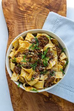 a bowl filled with pasta and meat on top of a wooden cutting board next to a knife