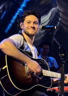 a man holding a guitar while sitting in front of a microphone and singing into a microphone