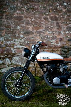 a white and orange motorcycle parked in front of a brick wall with moss growing on it