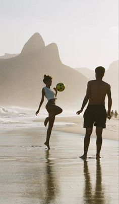 two people on the beach playing with a frisbee in the sand and mountains in the background