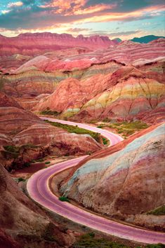 a winding road in the desert with colorful hills and mountains behind it at sunset or sunrise