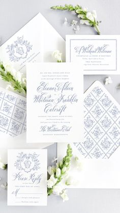 the wedding stationery is laid out on top of each other, with white flowers and greenery