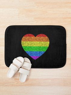 a pair of white slippers sitting on top of a bath mat next to a rainbow heart