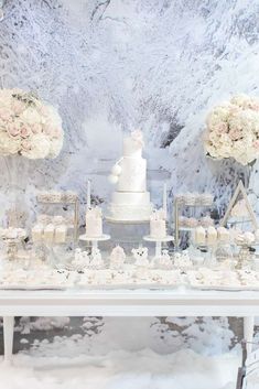 a wedding cake and cupcakes on a table with snow covered walls in the background