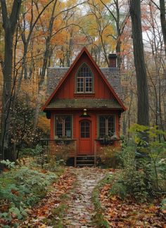 a small red house in the woods surrounded by trees and leaves with fall foliage around it