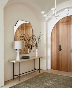 a room with a table, mirror and vases on the wall next to it