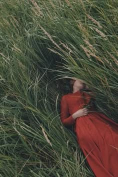 a woman in a red dress is laying down in tall grass