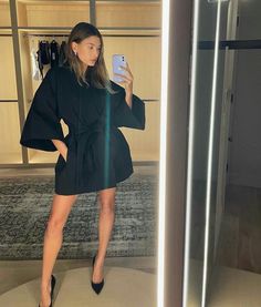 a woman taking a selfie in front of a mirror wearing a black dress and high heels