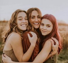 three young women hugging each other in a field