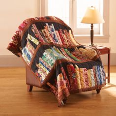 a chair with a quilt on it sitting in front of a table and lamp next to a window