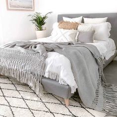 a bed with white sheets and blankets on top of it in a bedroom next to a potted plant