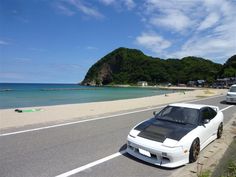 a white sports car parked on the side of the road next to the ocean and beach