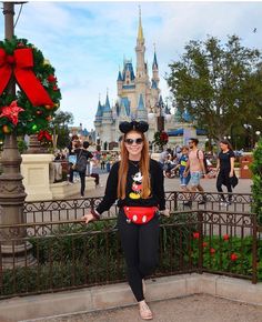 a woman standing in front of a castle wearing minnie mouse ears and mickey's hat